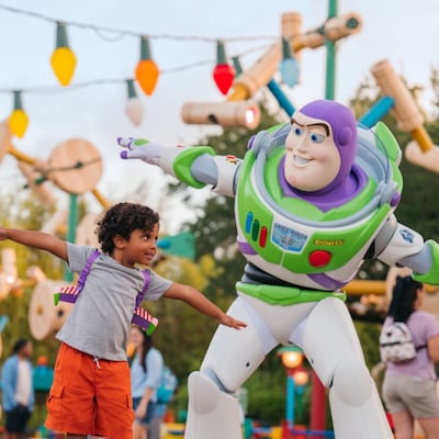 A young boy wearing space ranger gear standing next to Buzz Lightyear pretending to fly