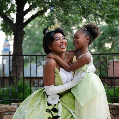 Una niña con un atuendo de la Princesa Tiana compartiendo un abrazo con la Princesa Tiana en Magic Kingdom Park