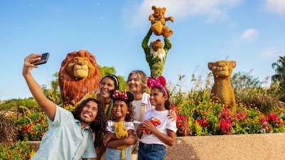 A family of 5 crowding together for a selfie in front of topiary versions of characters from The Lion King