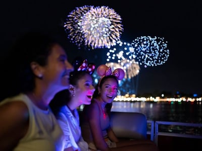 Three girls wearing Minnie Mouse ear headbands enjoying a nighttime fireworks display on a boat