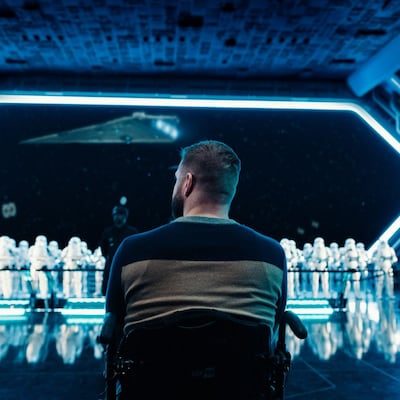 Um homem sentado em uma cadeira de rodas assistindo a stormtroopers na atração Star Wars Rise of the Resistance
