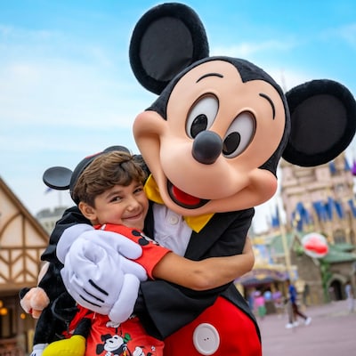 Un niño con un auriculares de Mickey Mouse abrazando a Mickey Mouse en Fantasyland de Magic Kingdom Park