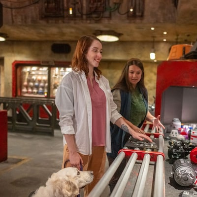 A woman reads the braille instructions for building a droid at the Droid Depot, while a female Cast Member looks on.