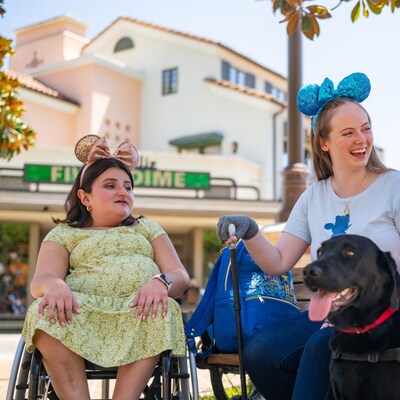 Una mujer en silla de ruedas, una mujer con un bastón y una mujer con un perro de servicio conversan mientras están sentadas afuera de Disney California Adventure Park.