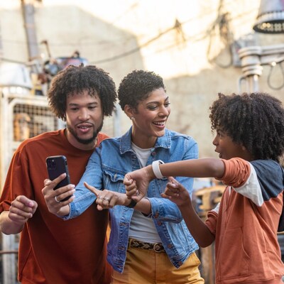 A child pointing at the Magic Band Plus on his wrist and 2 adults looking at a phone