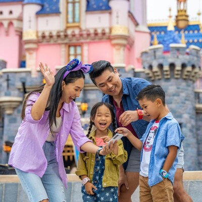 Dos adultos y dos niños con pulseras Magic Band Plus mirando un teléfono