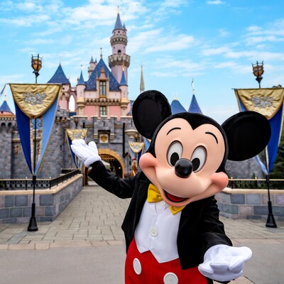 Mickey Mouse waving in front of a castle decorated with banners