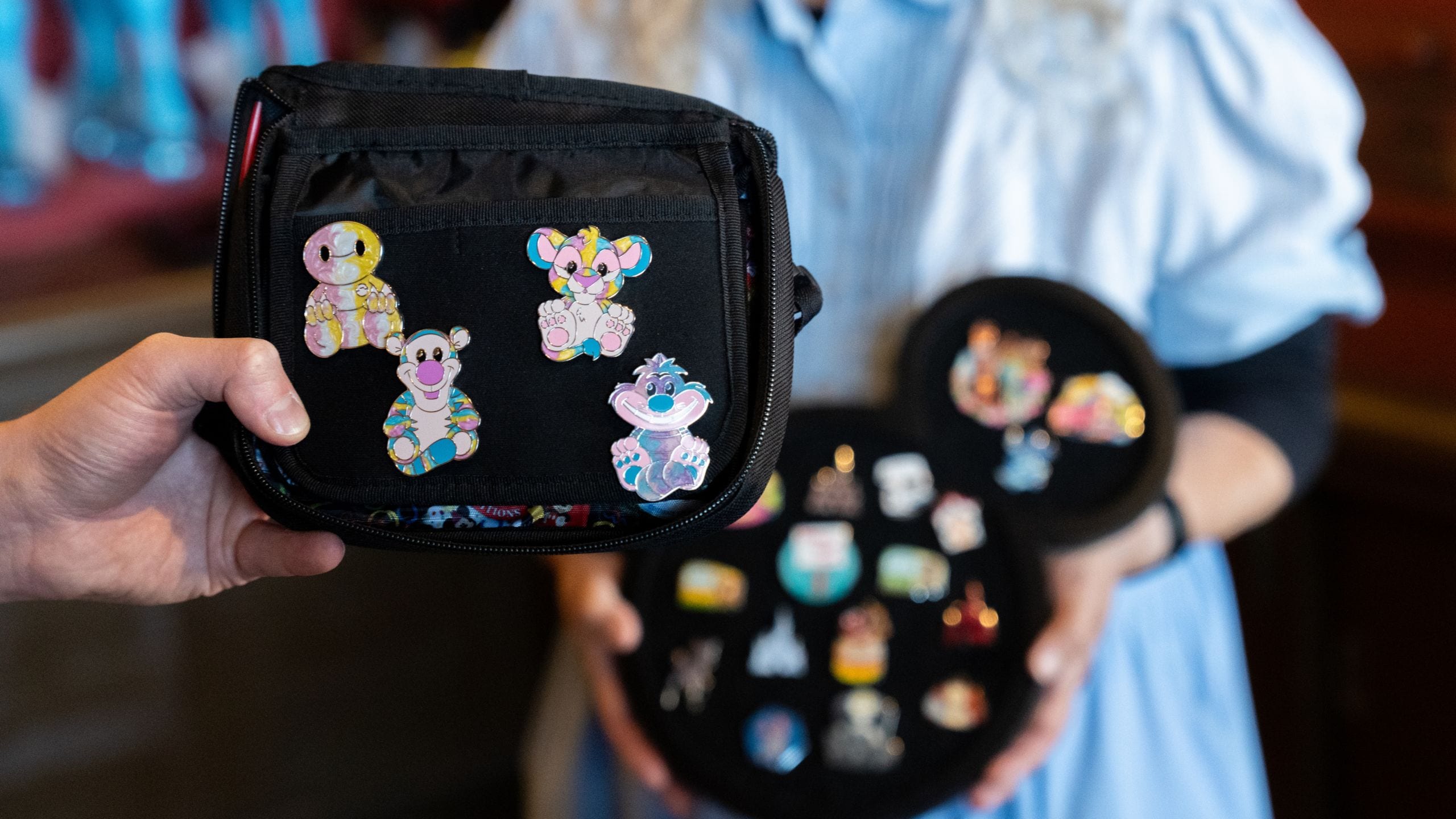 A Guest displaying a carrying case with pins in front of a Cast Member holding a pin trading board