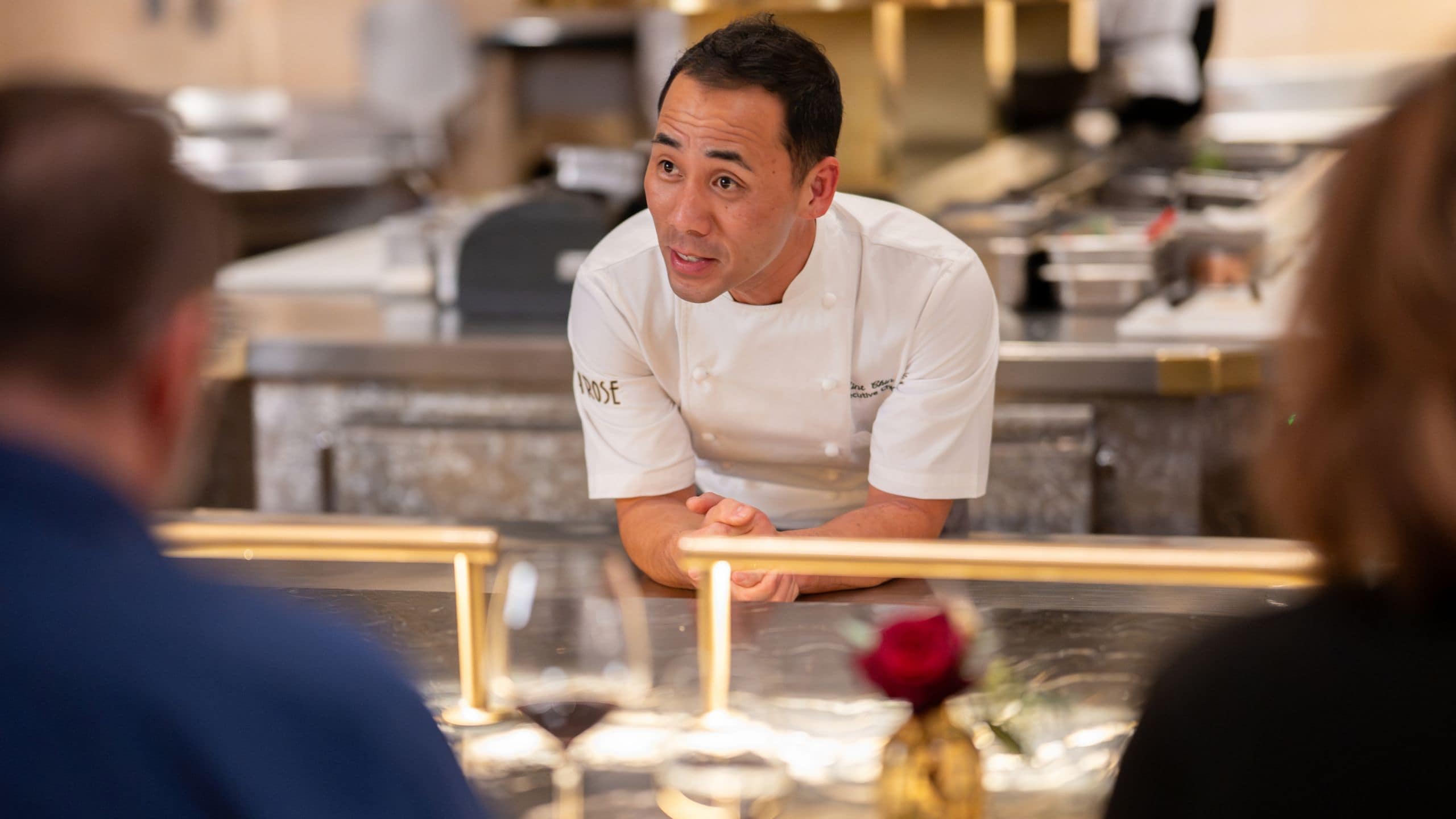 A chef talks to a customer dining at a restaurant counter in Napa Rose