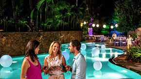 Guests socializing by a pool at an outdoor evening event with floating decorations and tables