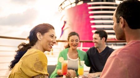 A group of adults sitting and drinking cocktails on the deck of the Disney Wish cruise ship