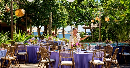 Disney Cast Member sets up outdoor dining tables with floral displays for a reception