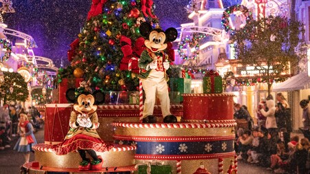 Mickey and Minnie ride a float with a Christmas tree and presents as snow swirls through the air