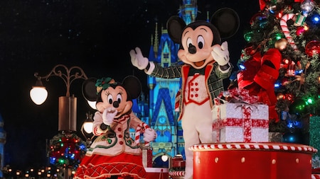 Minnie Mouse and Mickey Mouse standing on a Christmas themed parade float in front of Cinderella Castle