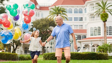 Un niño sostiene globos de Mickey Mouse mientras camina con un adulto en Disney’s Grand Floridian Resort & Spa