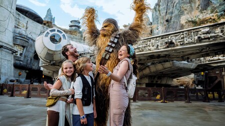 A family of 4 posing for a photo with Chewbacca at Star Wars Galaxy’s Edge in Disney’s Hollywood Studios