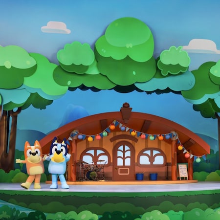 Bingo and Bluey pose on a stage set designed to look like a house in the woods at Bluey’s Best Day Ever