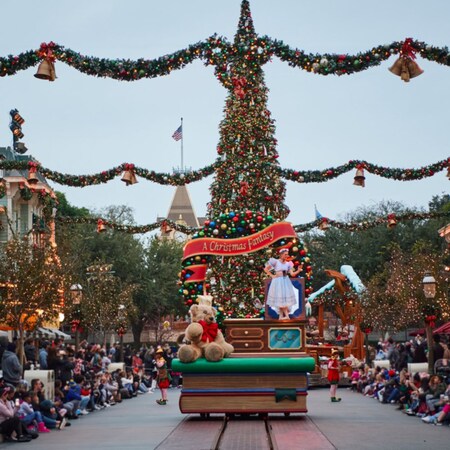 A ballerina and a giant teddy bear in front of a Christmas tree with a banner reading A Christmas Fantasy on a holiday themed parade float
