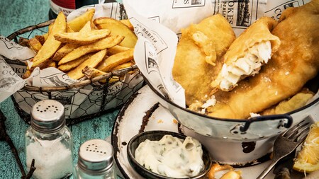 Uma refeição de peixe e salgadinho chips enrolada em um papel onde se lê Cookes of Dublin - o melhor peixe com salgadinho chips desde 1938, em inglês