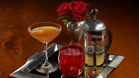 Tres bebidas servidas en una bandeja junto a un ramo de rosas