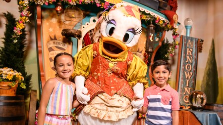 Daisy Duck is dressed as a fortune teller and she poses with a smiling little girl and boy