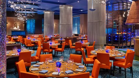 A modern restaurant with formally set tables, booths, decorative columns and abstract chandeliers that resemble underwater bubbles