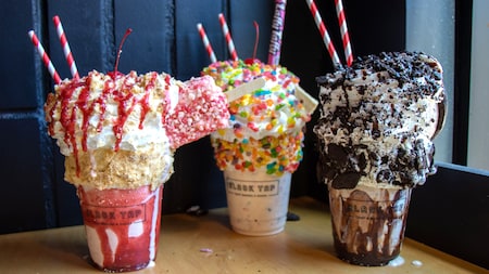 Una malteada de fresa con una barra de helado, una malteada de vainilla cubierta con caramelo y una malteada de crema y galletas