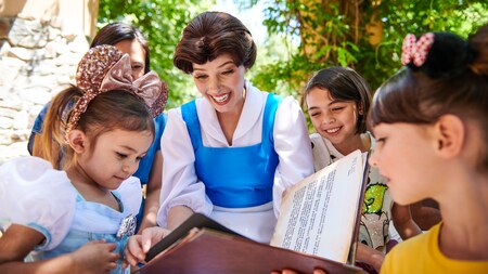 Disney Princess Belle is showing pages in a book to young girls