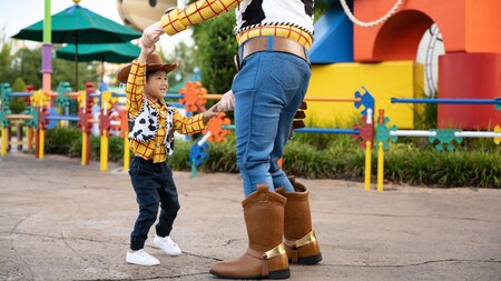 A child holding hands with Woody while dancing in Toy Story Land	