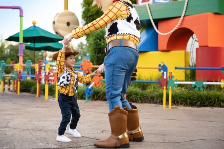 A child holding hands with Woody while dancing in Toy Story Land