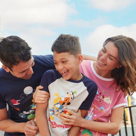 A boy and his parents wearing Walt Disney World tee shirts, laughing together near Cinderella Castle at Magic Kingdom park