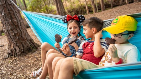 A little girl and 2 little boys sitting in a hammock, eating Mickey Mouse ice cream bars