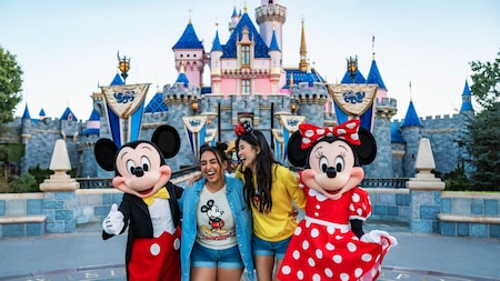 2 Guests pose with Mickey Mouse and Minnie Mouse in front of Sleeping Beauty Castle in Disneyland Park