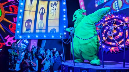 Guests wearing Halloween costumes watch Oogie Boogie dancing on stage. 