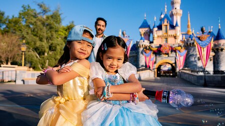 Two young girls in Disney Princess dresses strike a pose in front of Sleeping Beauty Castle at Disneyland Park