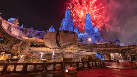 The Millennium Falcon docked in Star Wars Galaxy's Edge at night with fireworks lighting up the sky