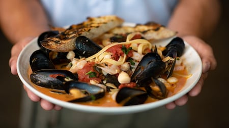 A server holding a bowl of pasta with mussels and shrimp