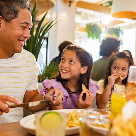 Two children smiling while eating at a table with an adult