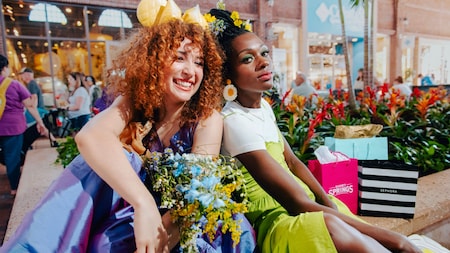Dos mujeres posan para una foto cerca de un jardín en un centro comercial.
