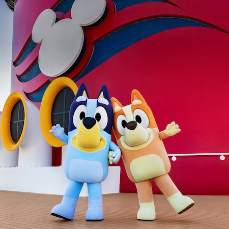 Bluey and Bingo standing next to a ship’s funnel on the top deck of a Disney cruise ship
