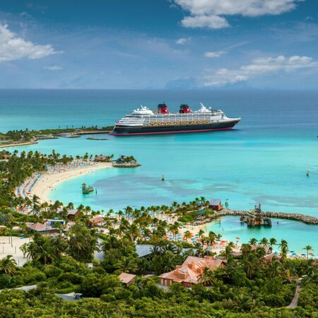 A Disney Cruise Line ship docked at Disney Lookout Cay surrounded by calm waters and sandy beaches lined with palm trees