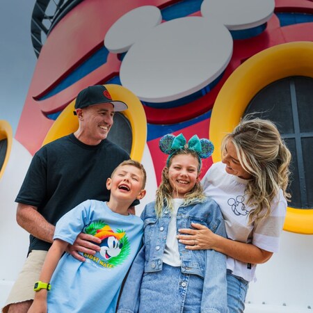 Family of 4 smiling in front of a Disney Cruise Line ship funnel with the Disney Cruise Line logo