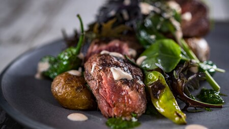 Hanger steak served with leafy greens and grilled peppers