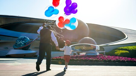 Holding Mickey Mouse themed balloons, a Disney VIP Tour Guide leads a small child to Mission Space