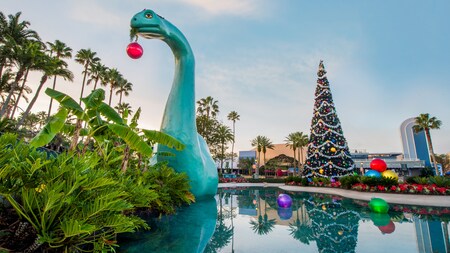 Gertie the Dinosaur rises above Echo Lake with a Christmas ornament hanging from her mouth and a Christmas tree nearby