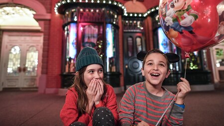 A boy holds a balloon while sitting on Main Street USA with his sister