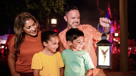A family of four in Fantasyland smile as they see Tinker Bell inside a lantern
