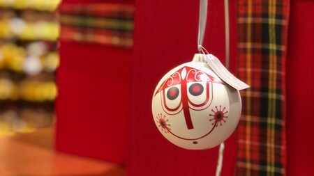 A Christmas ornament, decorated in the quirky style of Disney artist Mary Blair, hangs from a ribbon