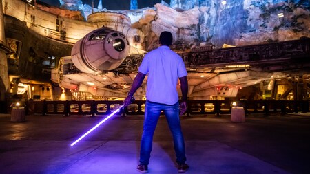A man holds a lightsaber while facing the Millennium Falcon