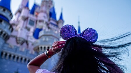 Girl stands in front of Cinderella's Castle at Disney World with purple mickey ears on